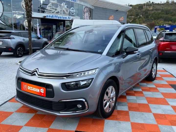 Citroën Grand C4 SpaceTourer gris acier mis en scène dans une vitrine de concession, logo encadré au mur - photo d'origine