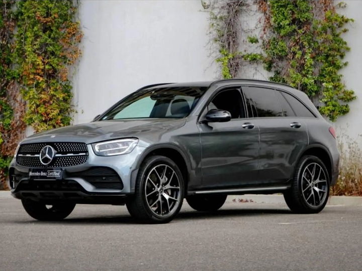 Mercedes-Benz GLC gris sélénite mis en scène dans un showroom sombre, logo de la concession au mur - photo d'origine